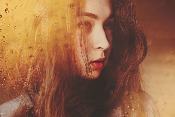 Atmospheric portrait of a moody female model posing by a window on a rainy day - examples of dark portraits