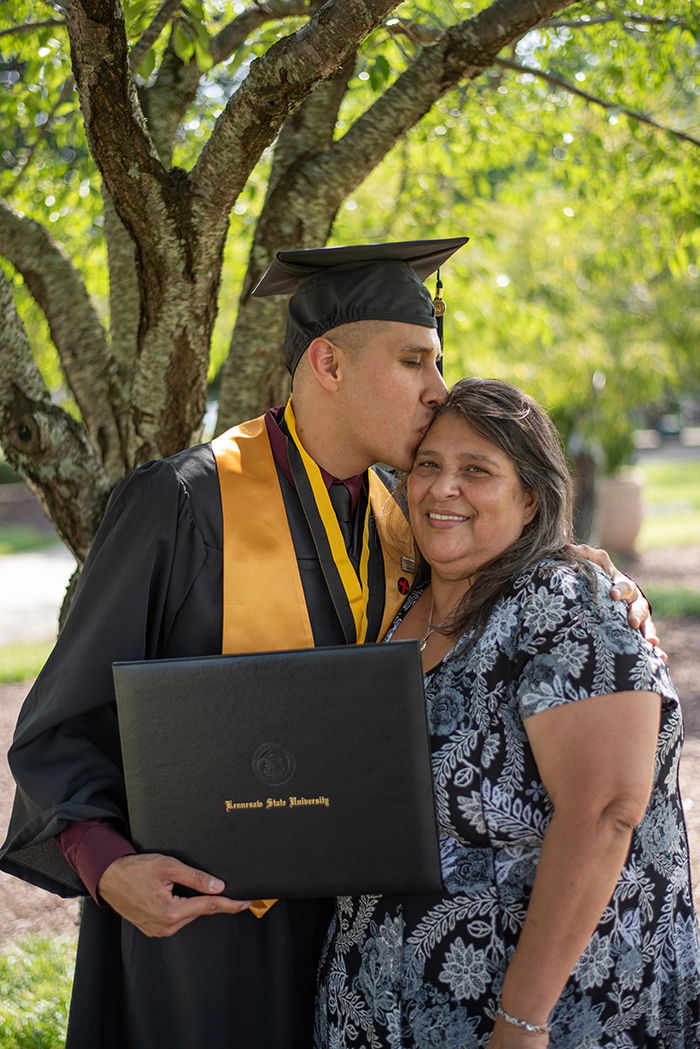 Beautiful graduation portrait of a male student embracing his mother outdoors