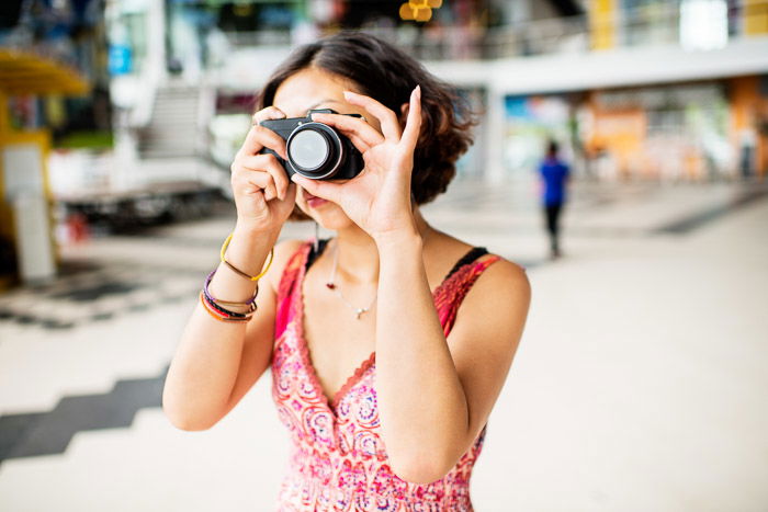 A female photographer holding a compact camera against a blurry background - grey market cameras