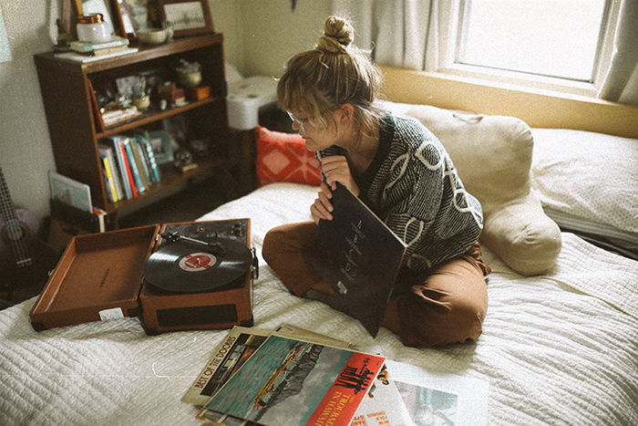 An analog photography portrait of a girl sitting on her bed choosing vinyl records to play in a cozy room - lifestyle portraits