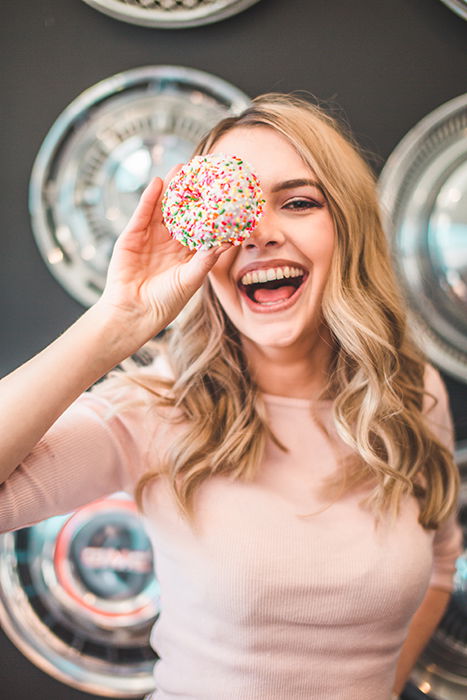 Fun portrait of a laughing female model holding a cake to her eye - how to smile for pictures