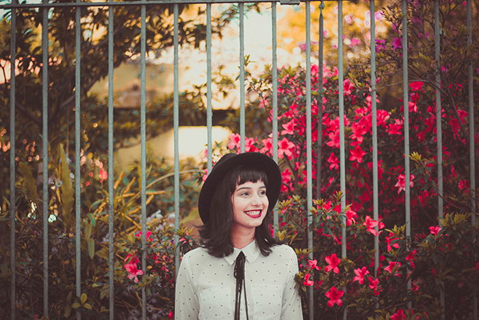 A female model standing outdoors in front of flowers and smiling naturally - how to smile in pictures