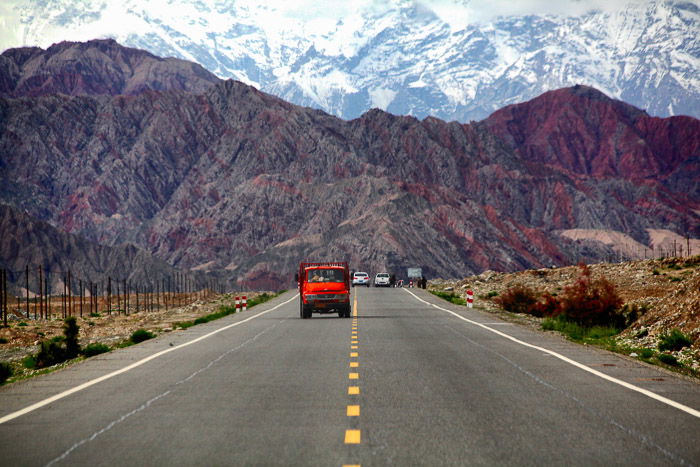 a red truck driving on a highway, a beautiful; mountainous landscape in the background - rule of space in photography