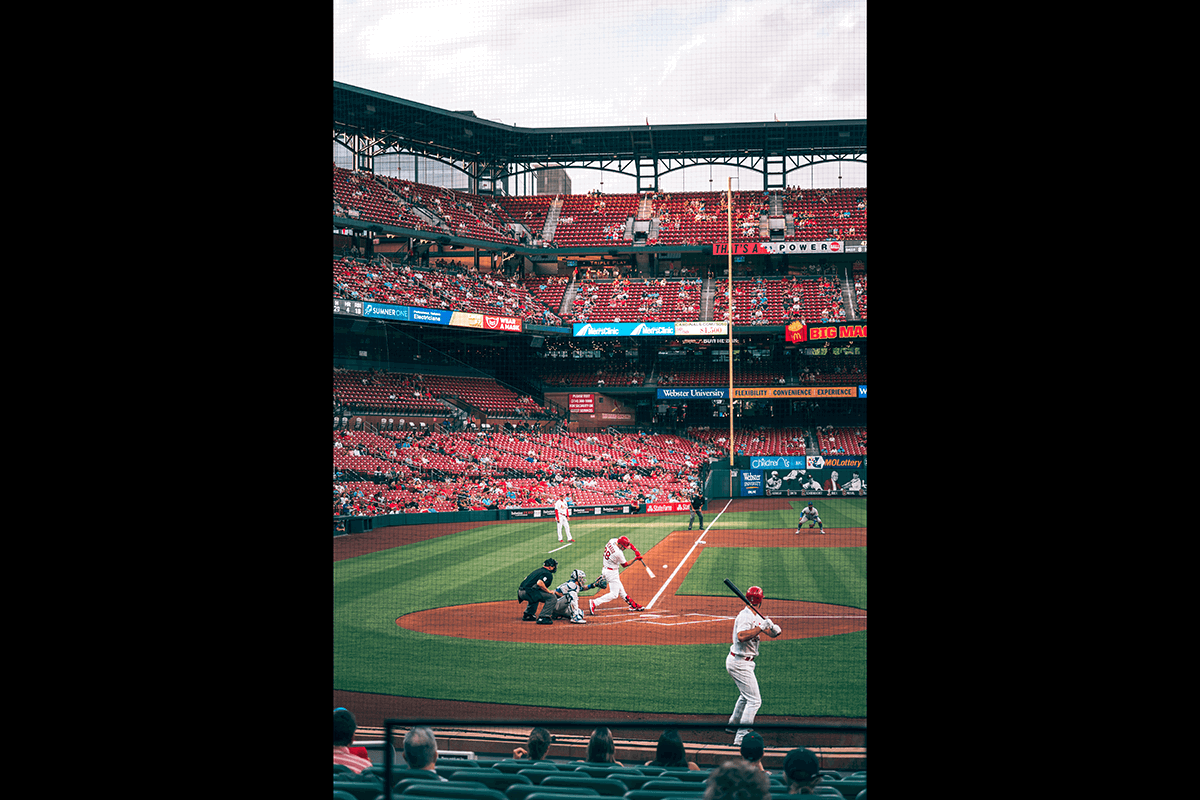 A wide shot of a stadium and field with a batter hitting a ball taken from the stands as an example for baseball photography