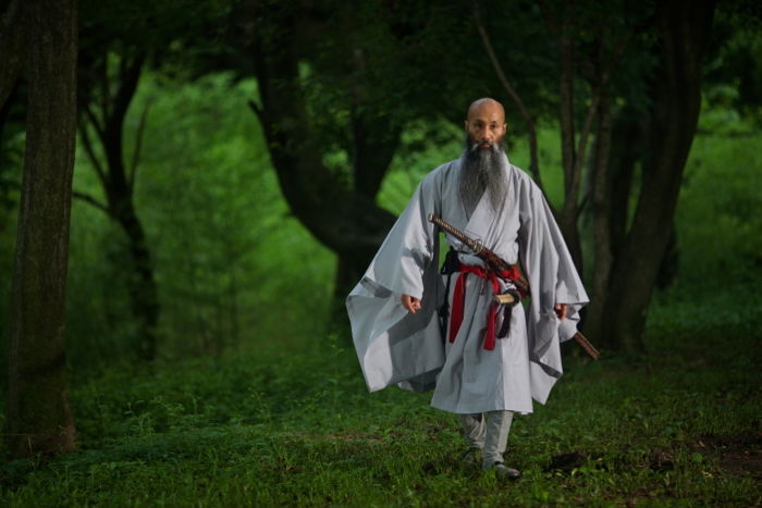 Atmospheric portrait of a monk lit by strobes in the dimly lit forest.