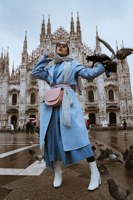 A female fashion model posing in front of a historical building with pigeons flying around her - fashion lookbook tips