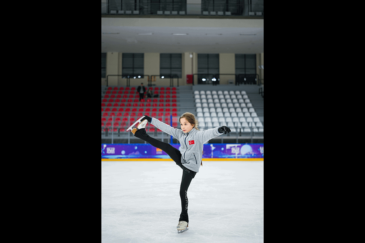 A child skate extending her leg holding onto her skate for a pose as an example of figures skating photography