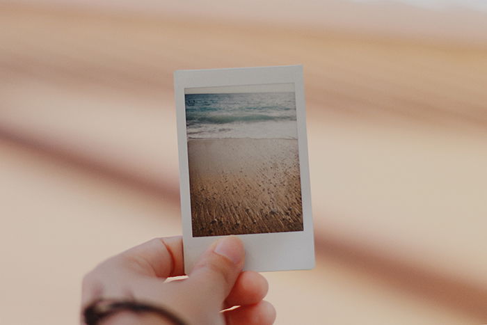 A persons holding an instant photo of a beach scene