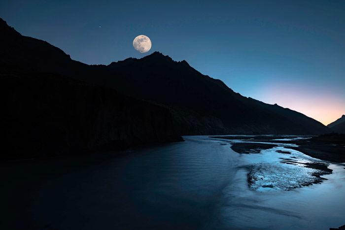 the moon above a beautiful mountainous landscape by a lake - stunning landscape photos 