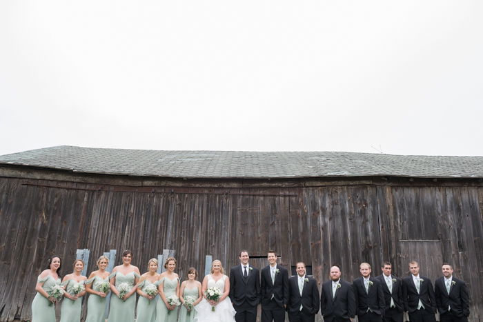 a wedding portrait of the wedding party posing in front of a rustic wooden building - wedding photography business tips