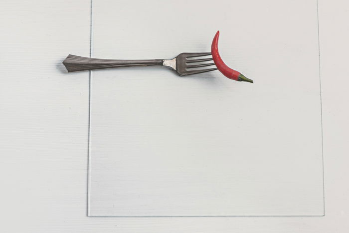 A chili pepper on a fork glued to a sheet of glass for a setup to shoot colorful paint in water photography