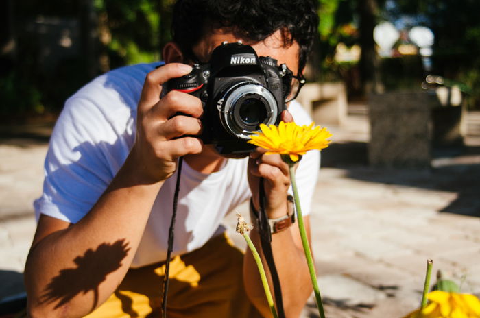 a man taking a macro shot of a yellow flower - macro photography lighting tips 