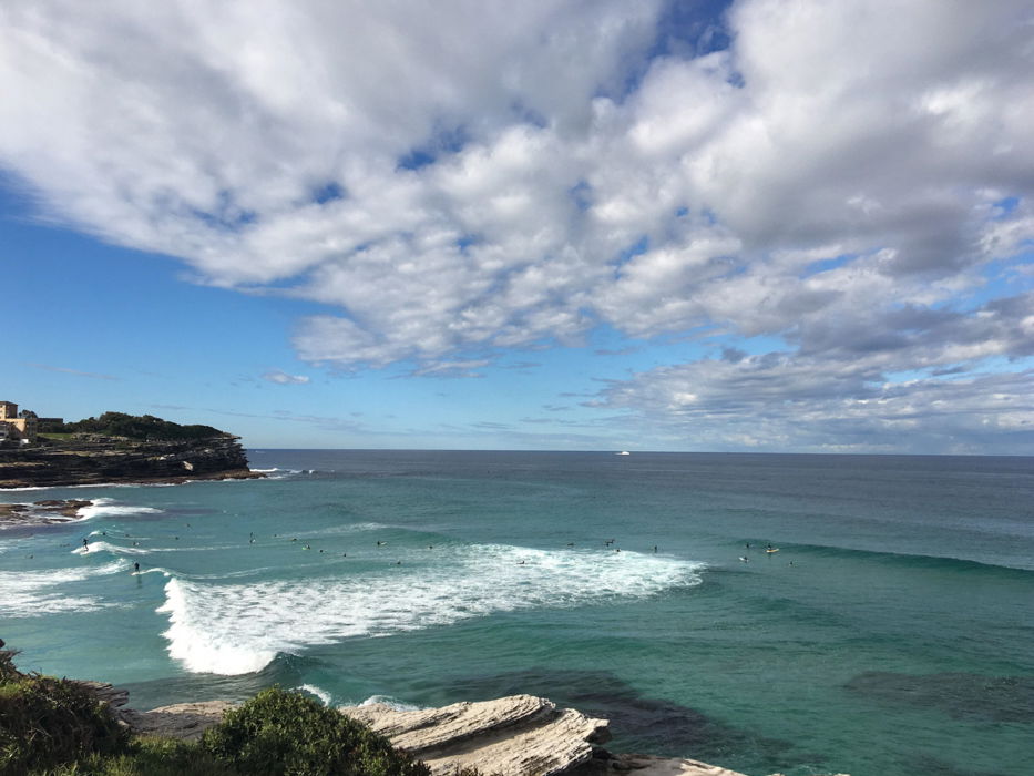 A seascape showing some land and waves with a blue sky with white clouds