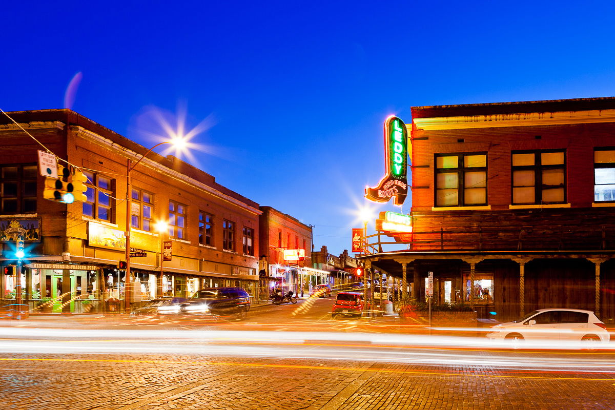 A bustling night scene in a city, with cars zooming by and bright lights from businesses lining the street. 