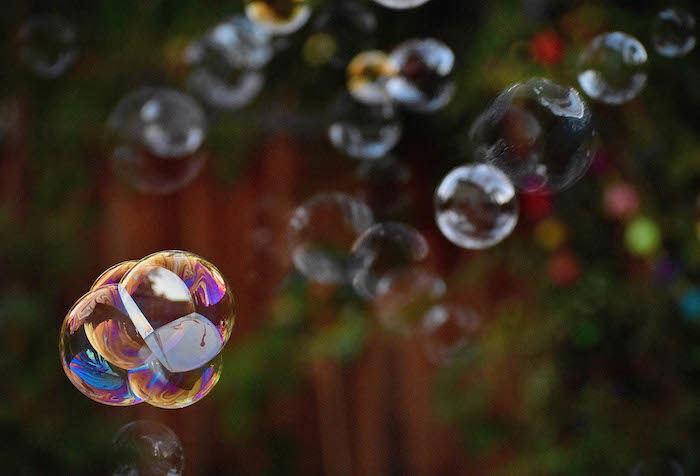 Clusters of bubbles with some color highlights floating in the air against a blurry landscape backdrop