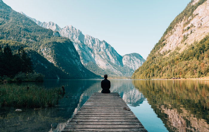 a lone figure sitting on a wooden pier by a lake, utilizing dynamic range in photography 