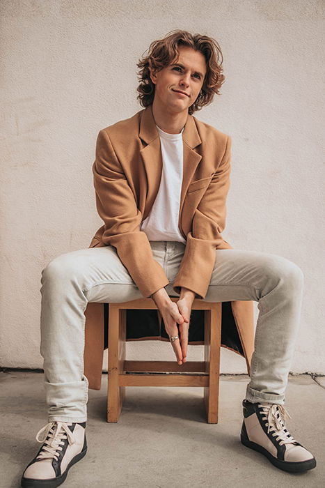 a minimalist portrait of a male model posed on a wooden chair indoors