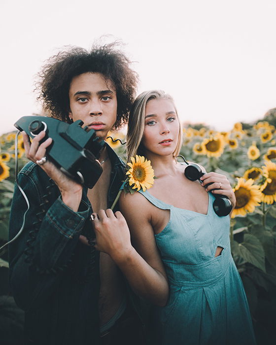 a minimalist portrait of a couple holding an old fashioned telephone in a sunflower field