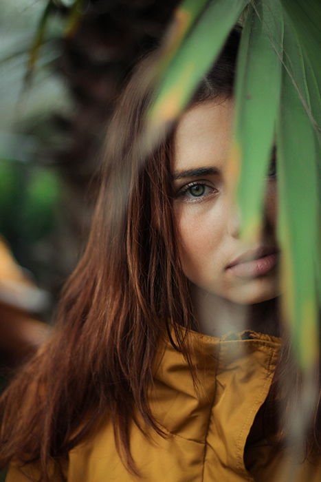 a minimalist portrait of a female model with green leaves in the foreground