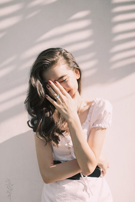 a minimalist portrait of a female model covering her laughing face with her hand