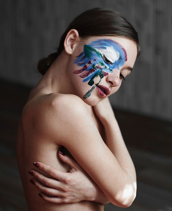 Artistic nude photography of a female model with paint on her face