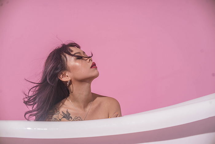 A woman sitting in a bathtub with her eyes closed and looking up as an example of nude photography