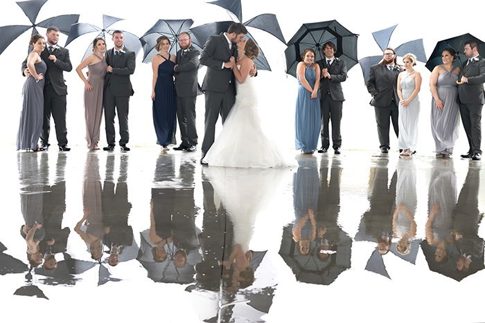 a group wedding shot of the bridal party holding umbrellas in the rain