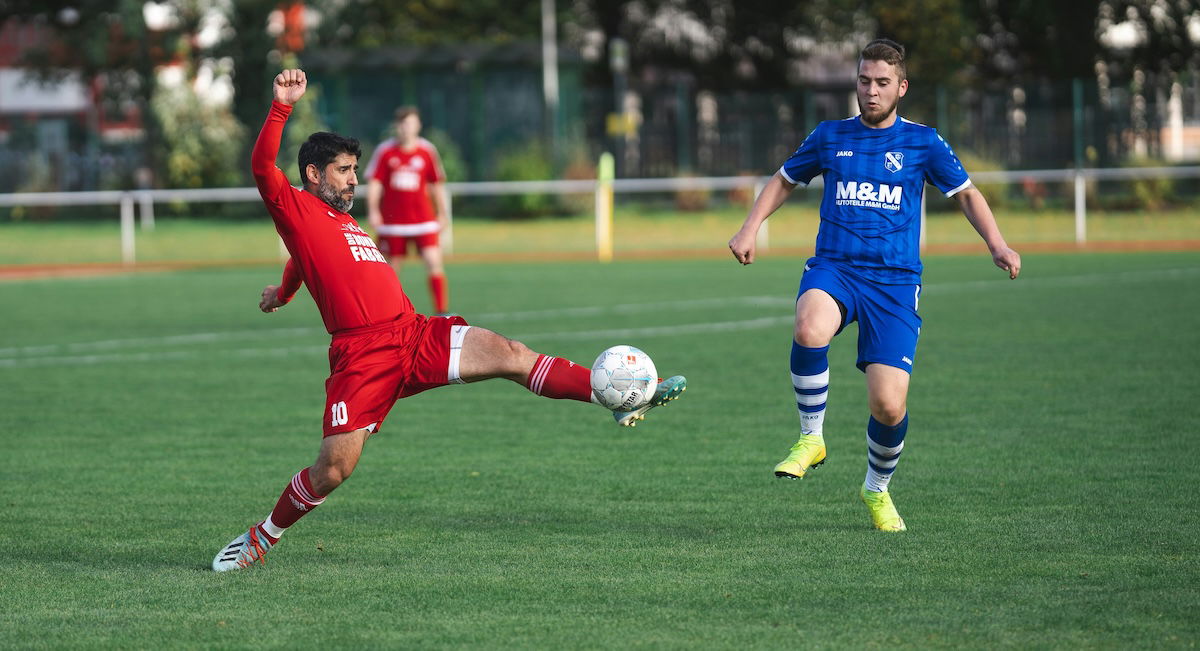 A player stretching out to kick a ball with another looking on as an example of soccer photography