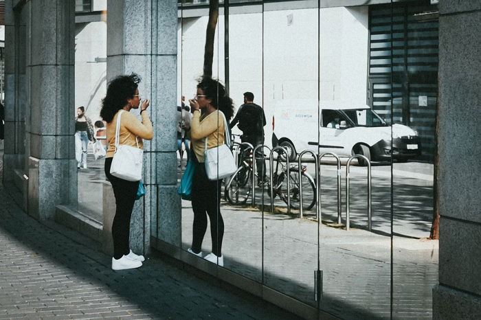 Street photography shot of woman doing makeup in reflection of a glass wall