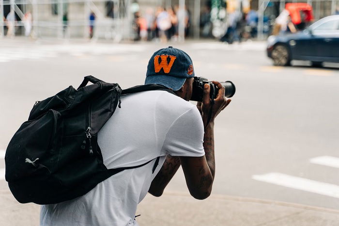 Man in plain clothes bending down to take a picture in the street