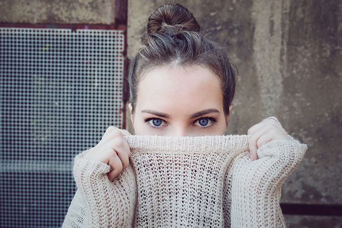 Portrait photo of a woman with blue eyes pulling her sweater in front of her mouth