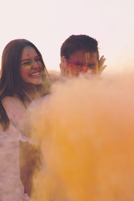 Photo of a girl and a boy with simple background behind yellow color powder