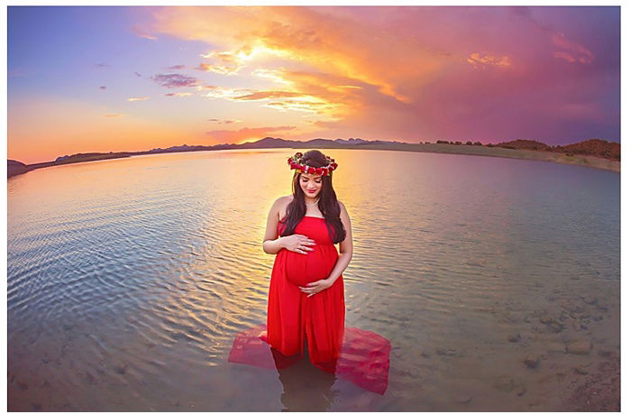 Photo of a pregnant woman standing in the water at sunset