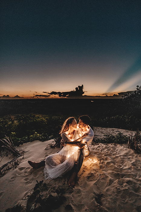 atmospherically lit outdoor portrait of a couple posed on a beach with fairy lights