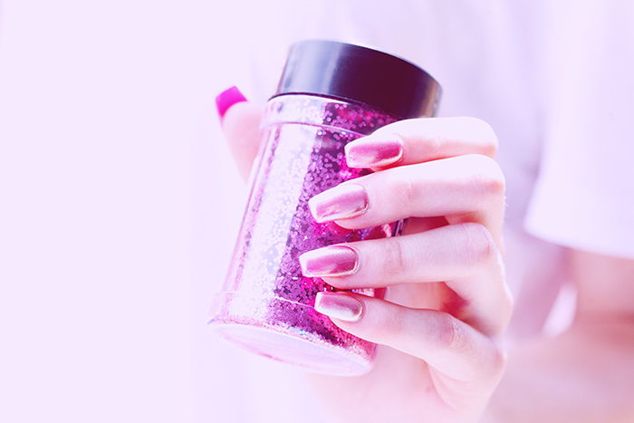 cool nail photography of a female model with painted nails holding a tub of glitter