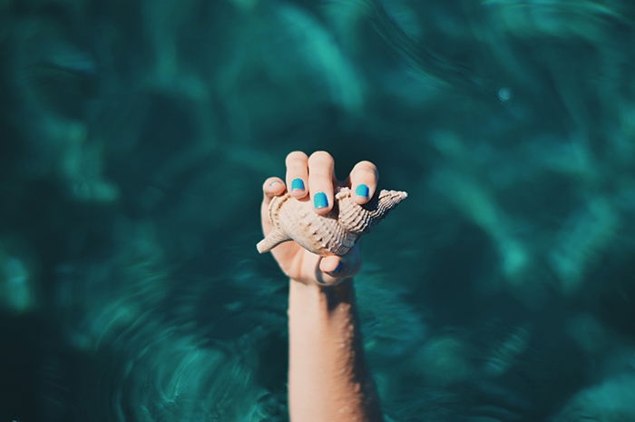 cool nail photography of a female model with painted nails holding a seashell 