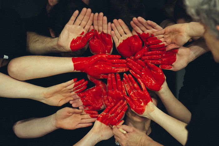 Photo of many pairs of hands painted red forming the shape of a heart