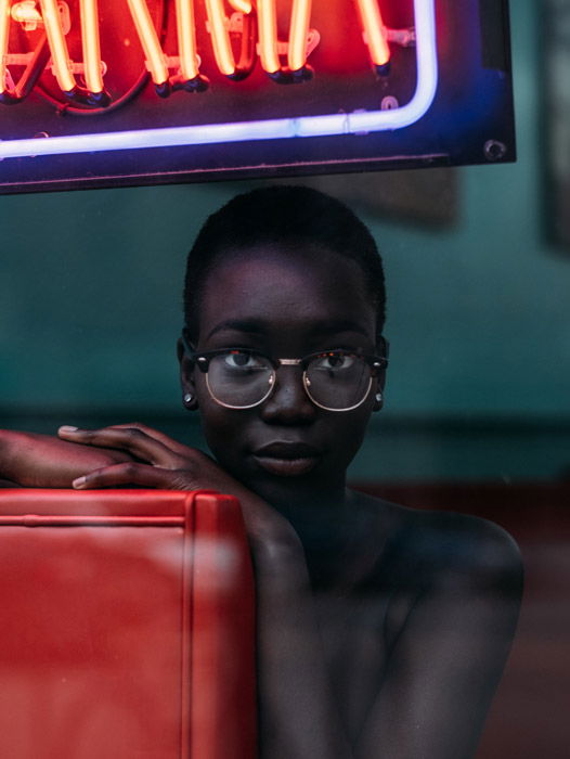 Portrait photo of a woman with glasses sitting on a red sofa behind a restaurant window