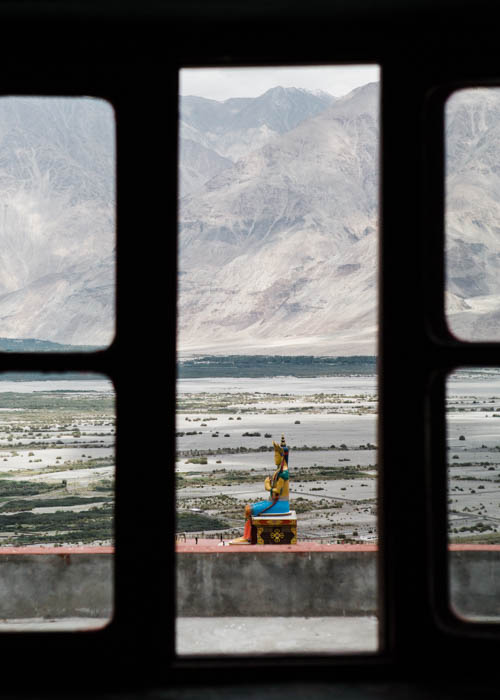 Photo of a buddhist statue shot from a window with mountains in the background