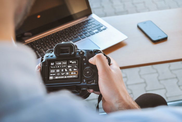 Photo of a man changing the settings of a camera with a computer in the background