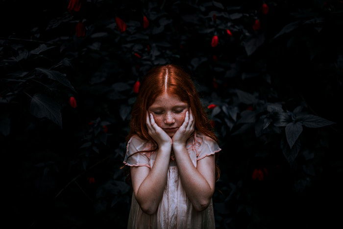 Low key lighting used to capture a photo of a re-haired girl in front of a bush