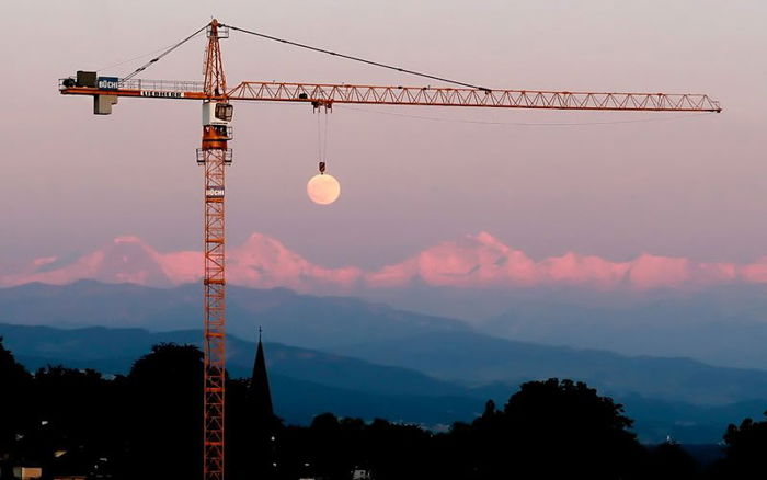 Photo of a crane holding the moon in the background