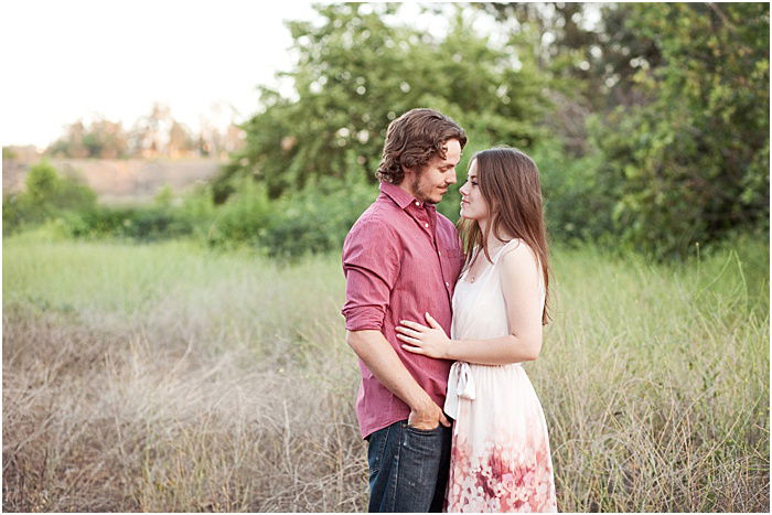 A couple is seen standing in a field with tall grass, sharing an intimate moment as they gaze into each others eyes. 