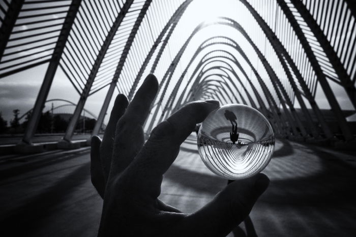 a hand holding a small lensball reflecting a black and white street photo 