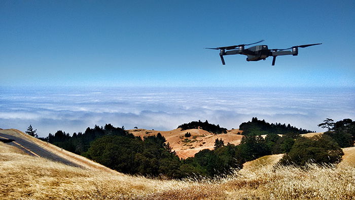 A drone with a camera flying over a hilly landscape over clouds for time-lapse photography