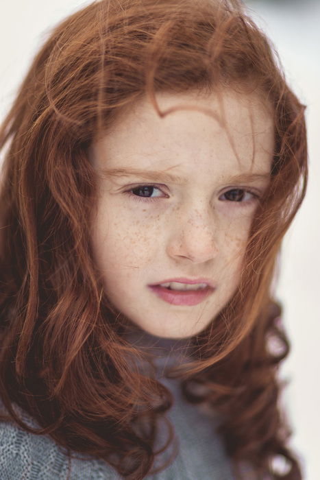 A young girl with red hair and freckles is staring at the camera. 