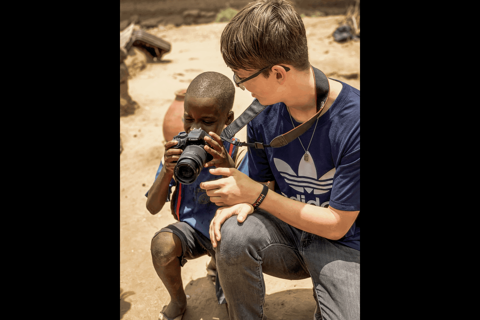 A teenager showing a kid how to use a camera with a zoom lens to show photography for kids