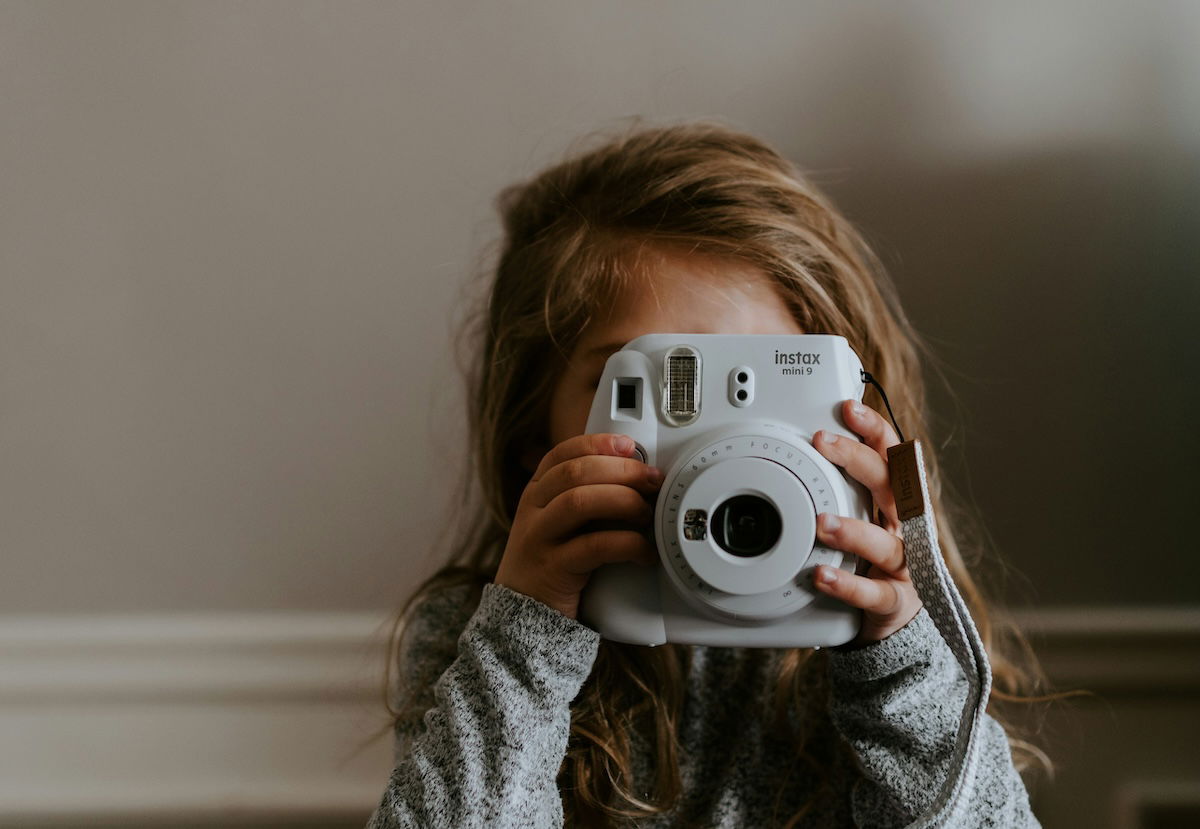 A girl holding up an instant camera to her face to show photography for kids