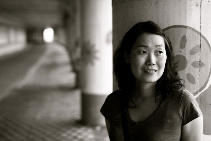 black and white portrait of a girl standing against a stone column