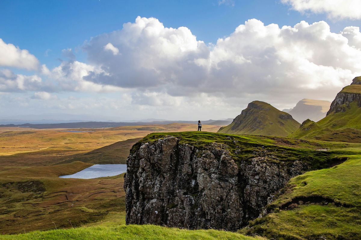 Stylized landscape with a person on a cliff beneath white clouds and blue sky as an example of photography style